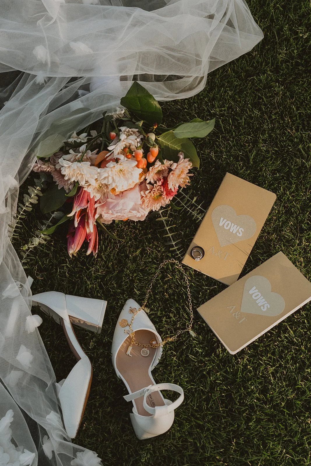 Wedding vow books, white shoes, bouquet, veil, and rings arranged on the grass at Skamania Lodge.