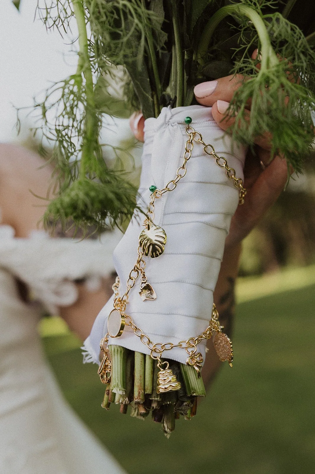 Close-up of a wedding bouquet wrapped with a gold charm bracelet and white ribbon.