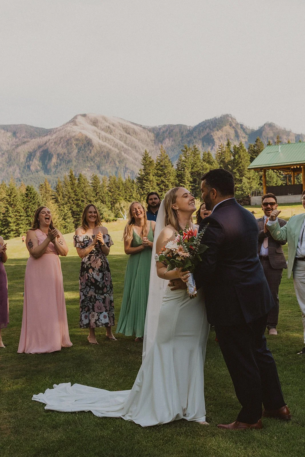 Wedding guests cheering as the newly married couple celebrates after their ceremony with Columbia River Gorge mountains in the background at Skamania Lodge.