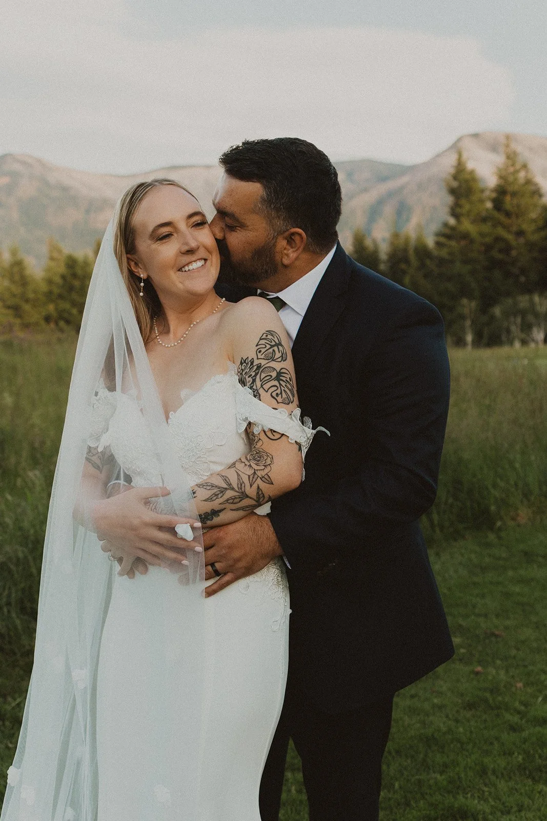 Groom kissing the bride's cheek during golden hour wedding portraits at Skamania Lodge with Columbia River Gorge mountains behind them.
