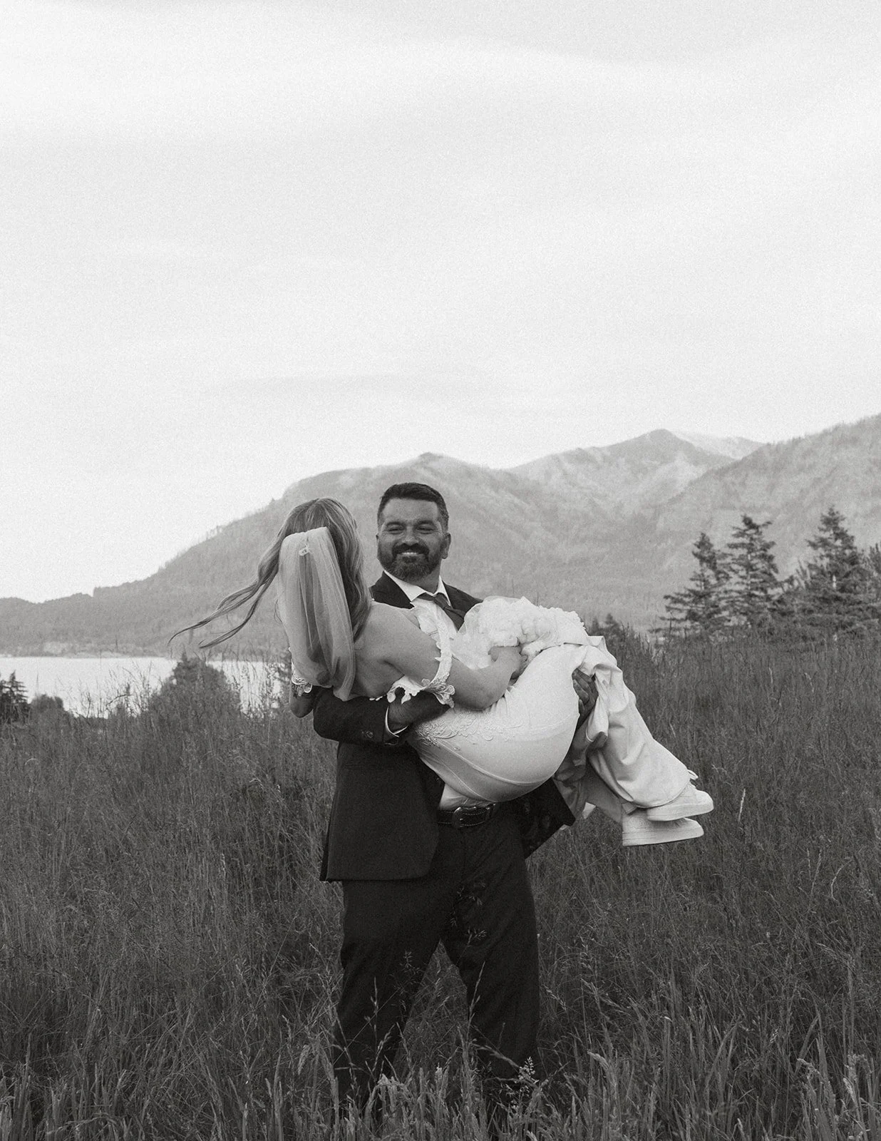 Groom carrying his bride through a meadow with Columbia River Gorge mountain views during portraits at Skamania Lodge.