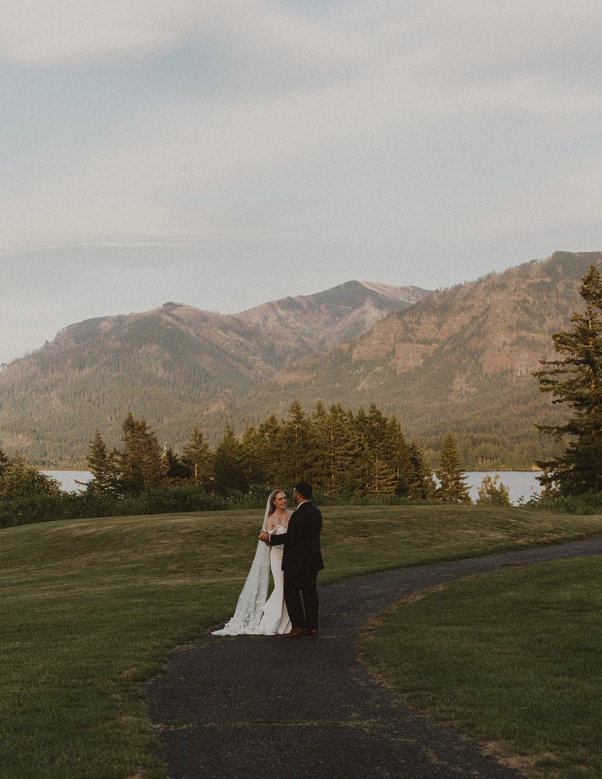 Bride and groom standing together on a winding path with Columbia River Gorge mountain views during sunset portraits at Skamania Lodge.