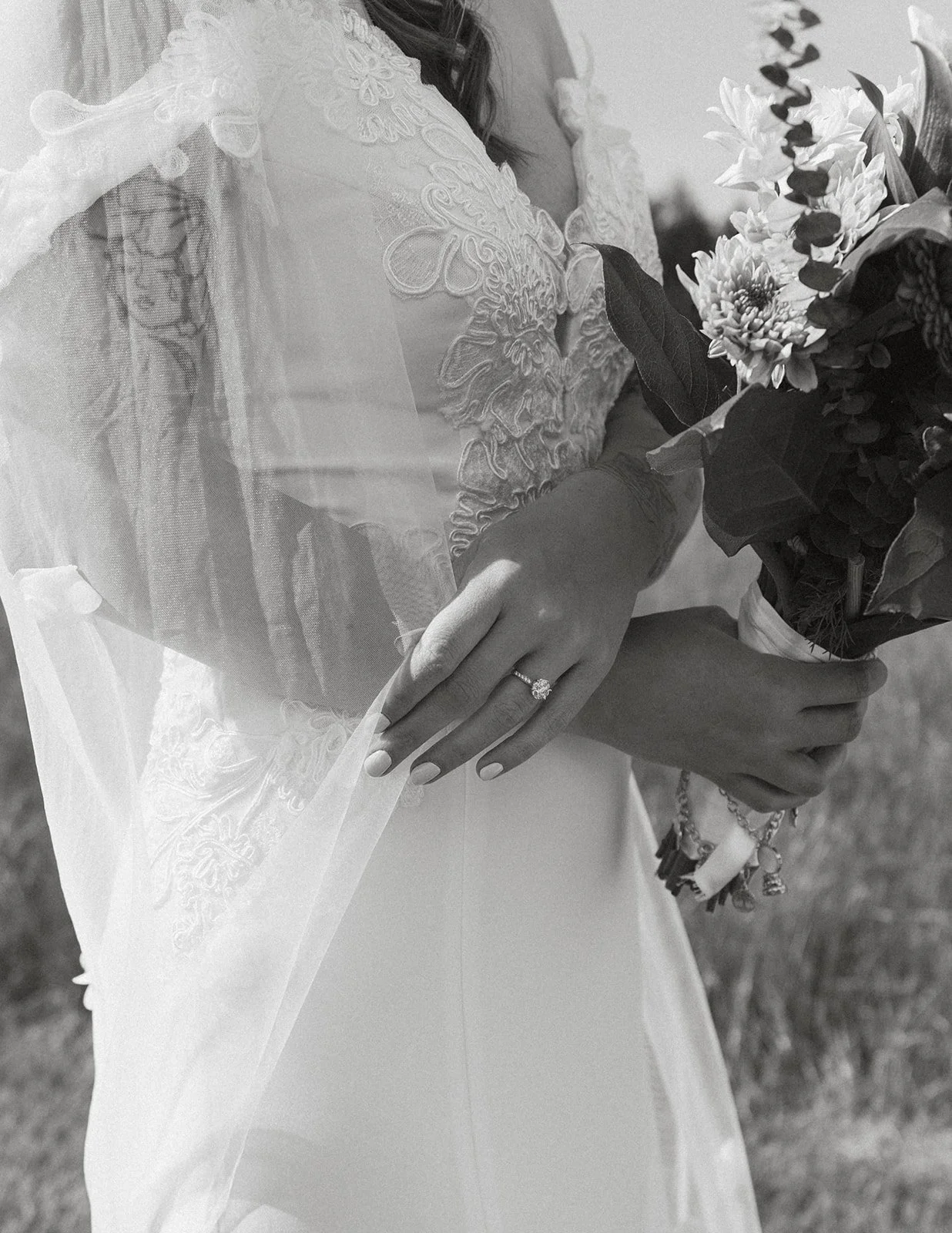 Black-and-white detail of a bride holding her bouquet and showing her engagement ring.