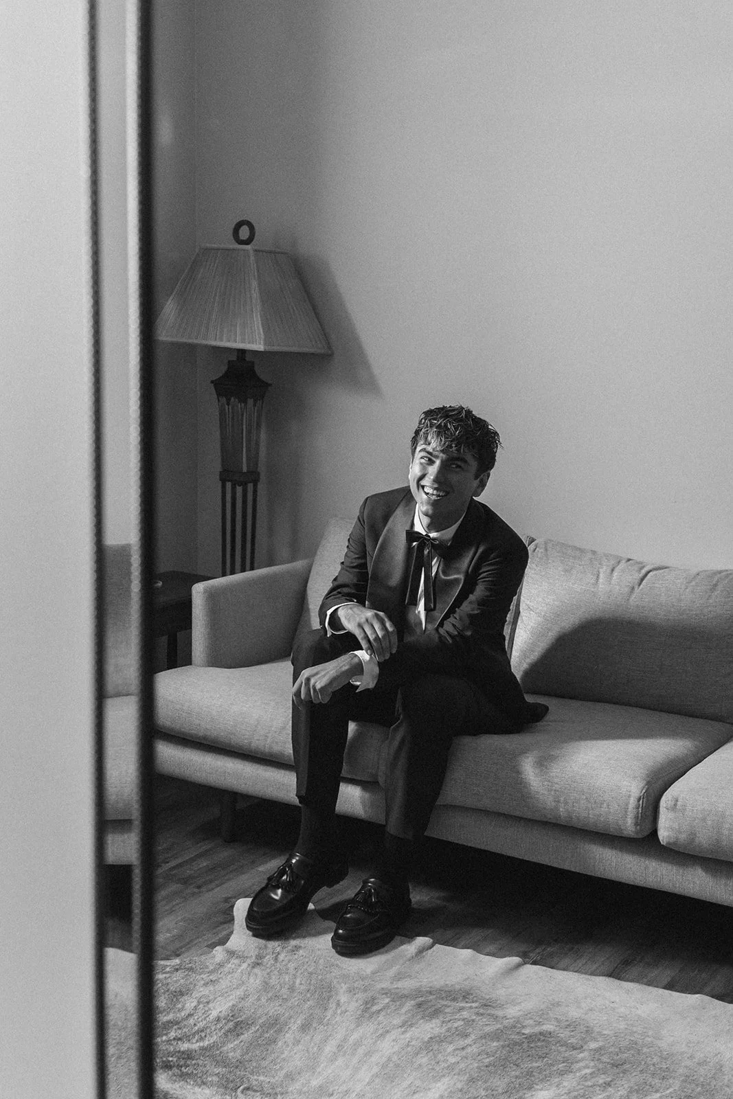 Groom smiling while seated on a couch in the groom's suite before the ceremony at Bright Morning Farm.