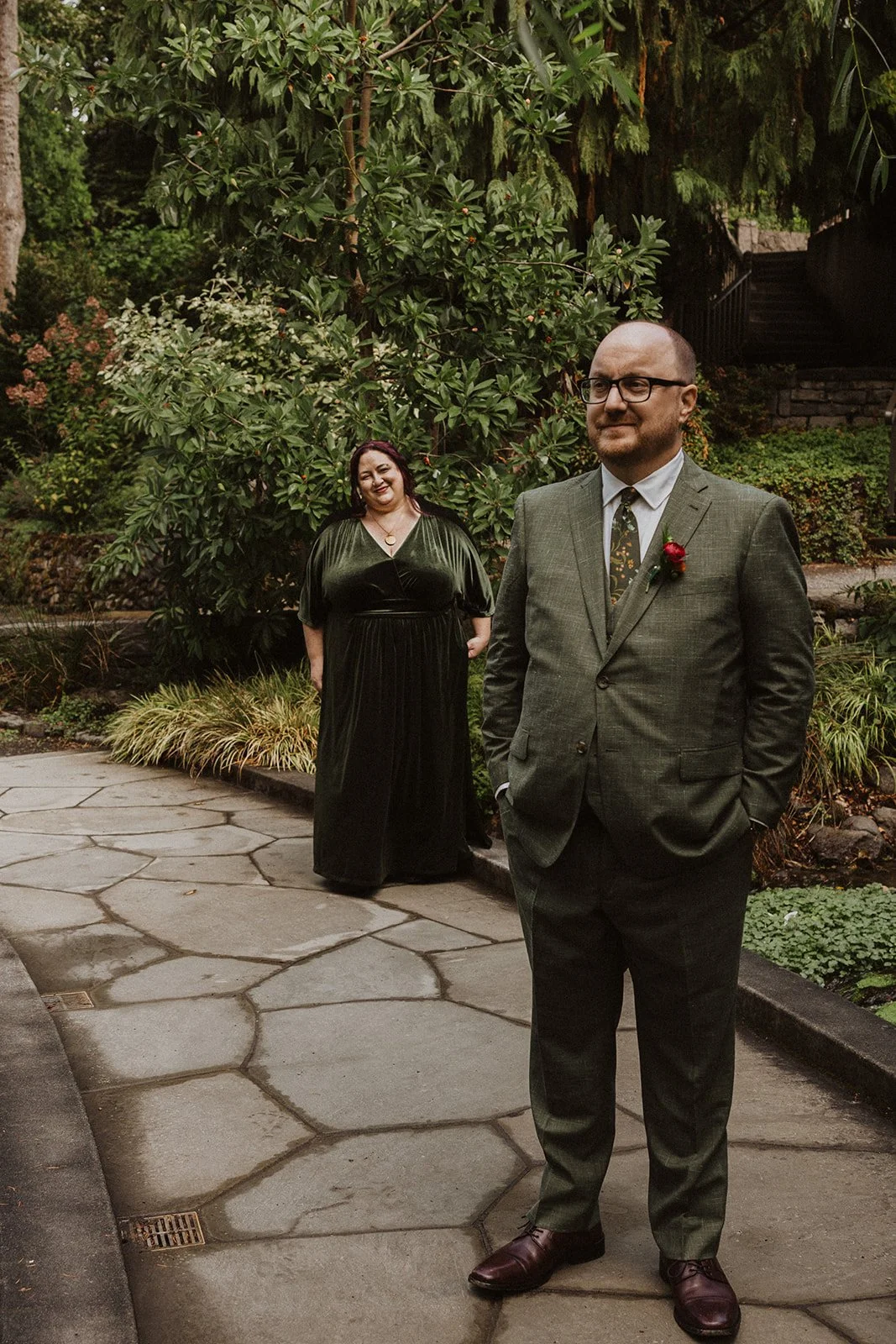 Groom waits on a stone path under willow branches before the first look