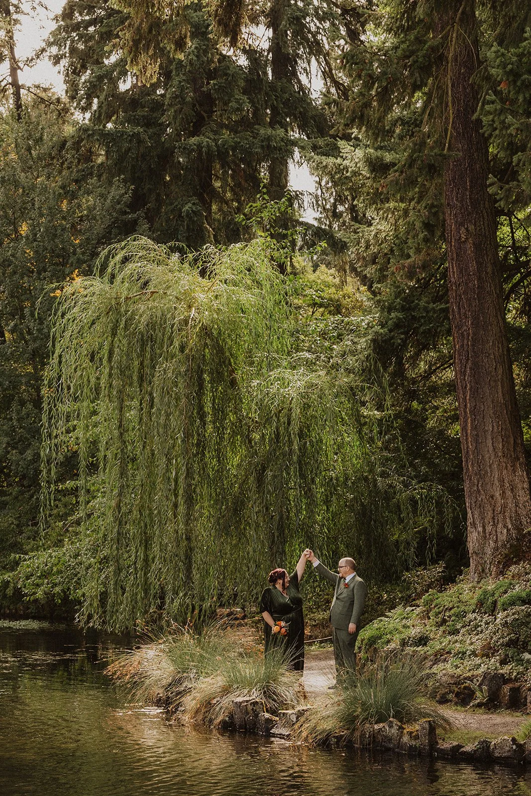 Couple embracing under a weeping willow at their Crystal Springs Rhododendron Garden wedding