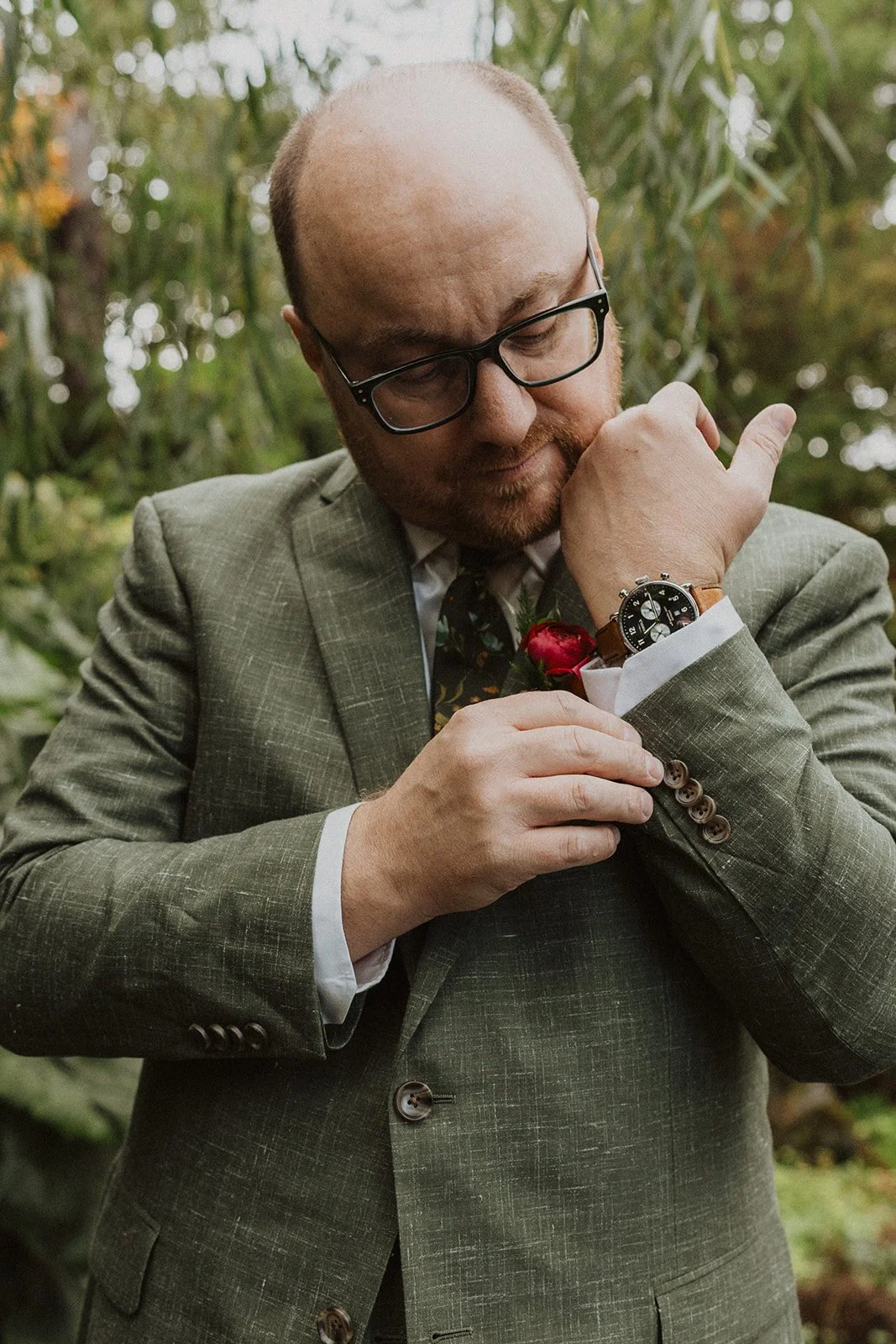 Groom adjusts his shirt cuff and watch before an Oregon garden wedding ceremony