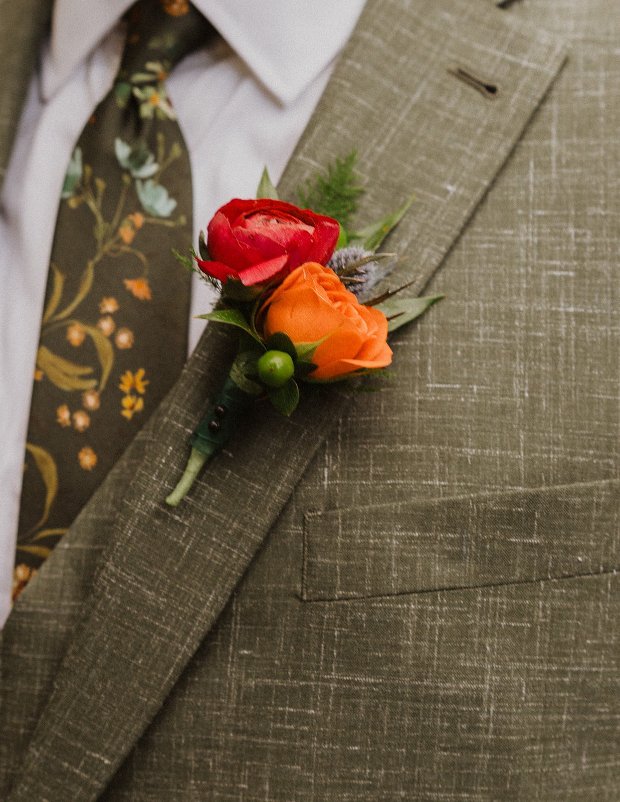 Green linen suit with a floral tie and a red ranunculus boutonniere