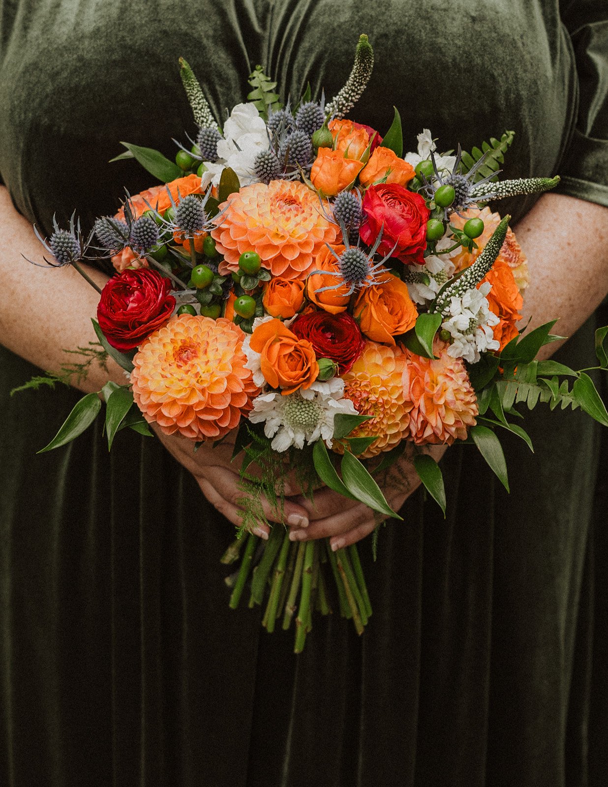 Dahlias, ranunculus and blue thistle in a bouquet against forest green velvet