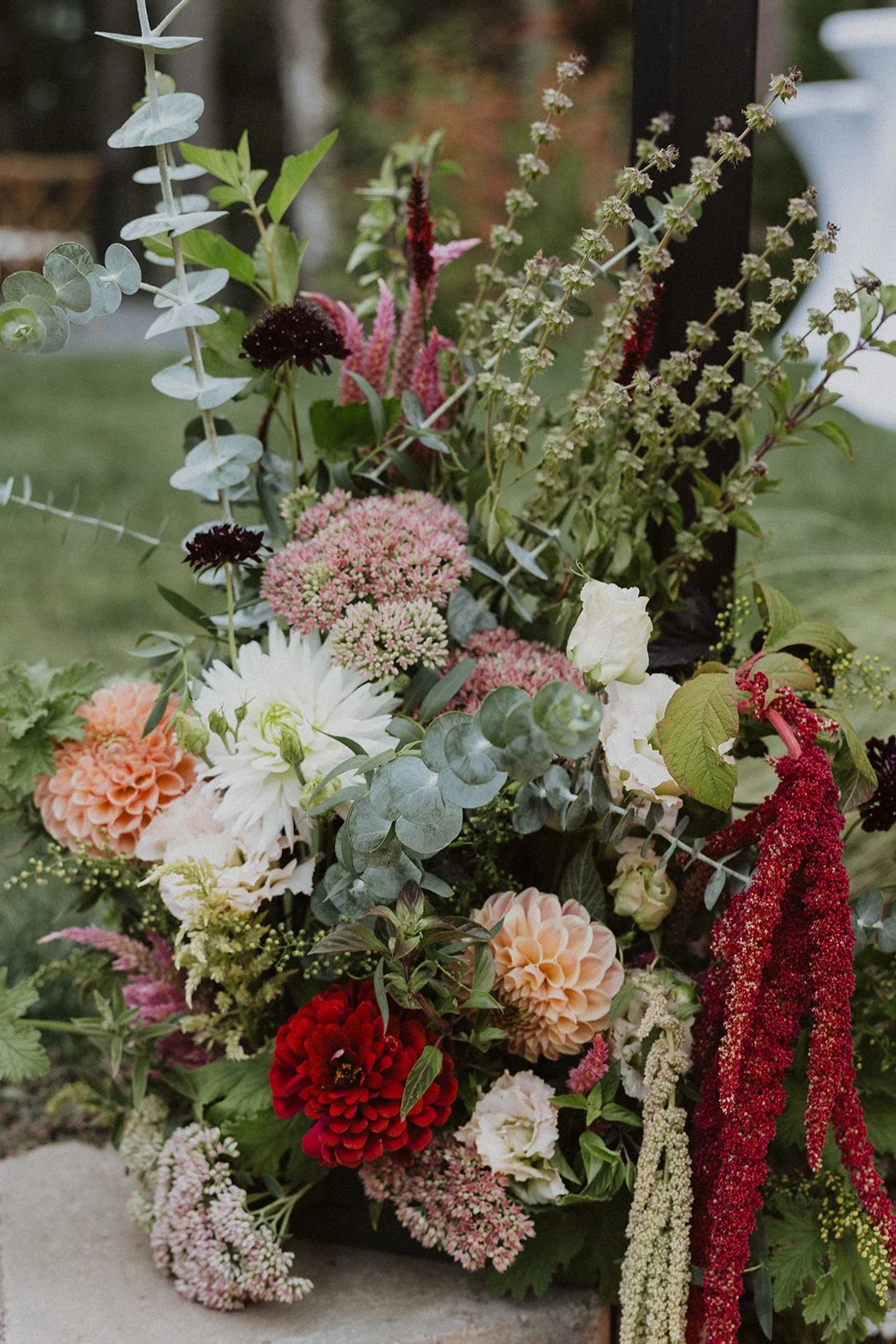 Garden grown ceremony florals in reds and peach against a dark post