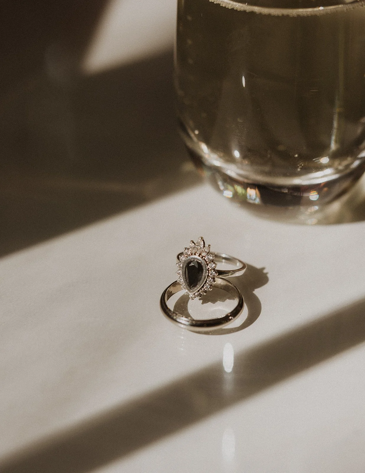 Wedding rings in hard morning light beside a champagne glass