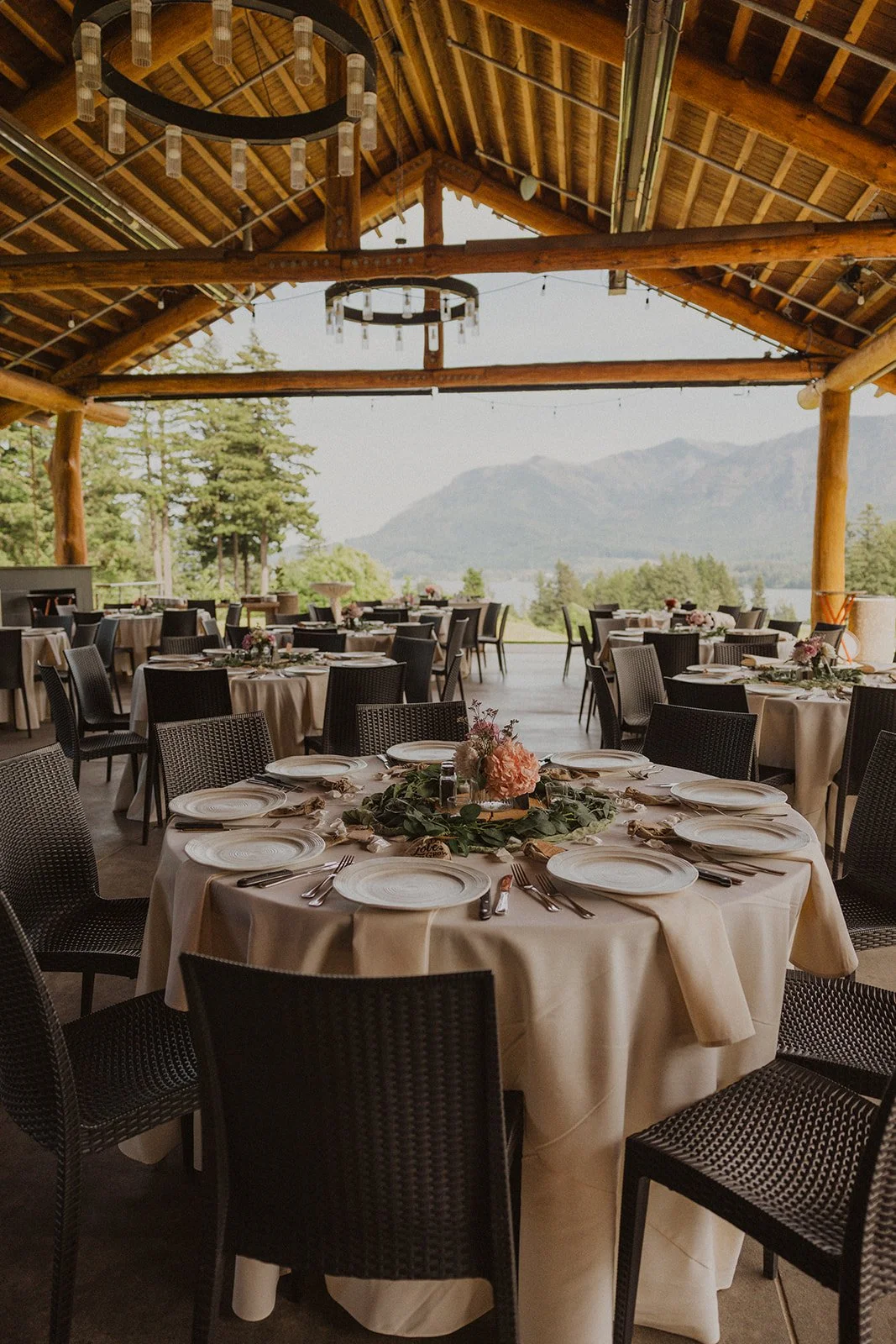 Round tables set under a timber pavilion with chandeliers and open sides