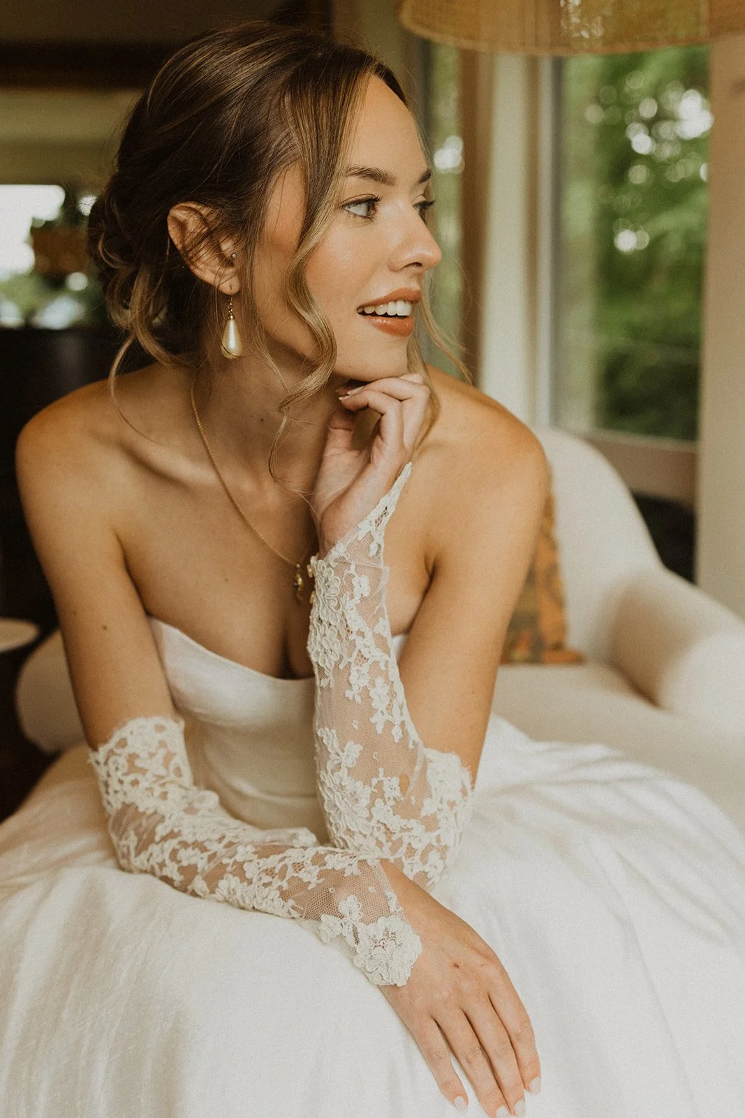 Seated in lace gloves beside a window with green trees outside