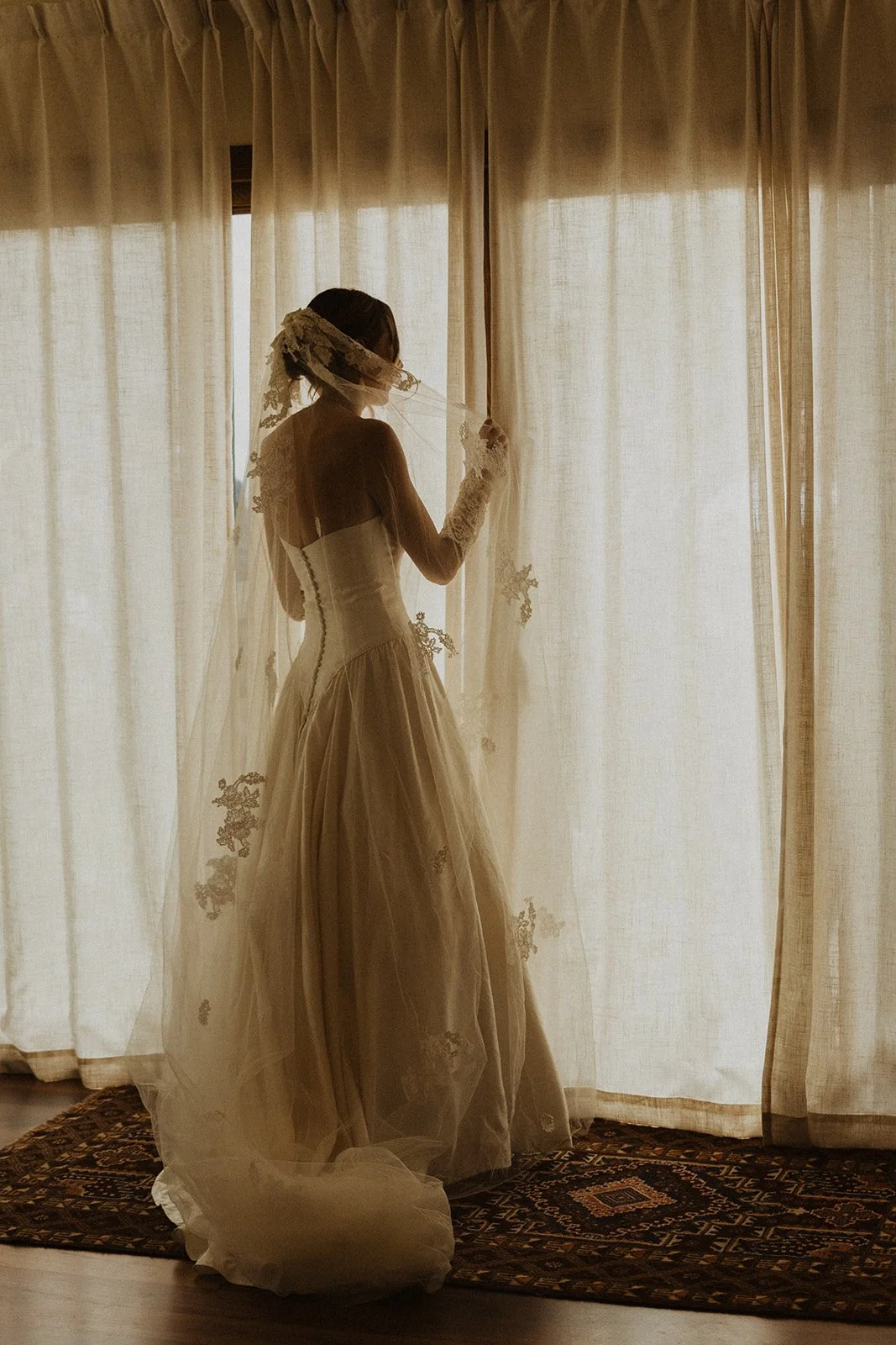 Backlit at a curtained window wearing a long lace trimmed veil