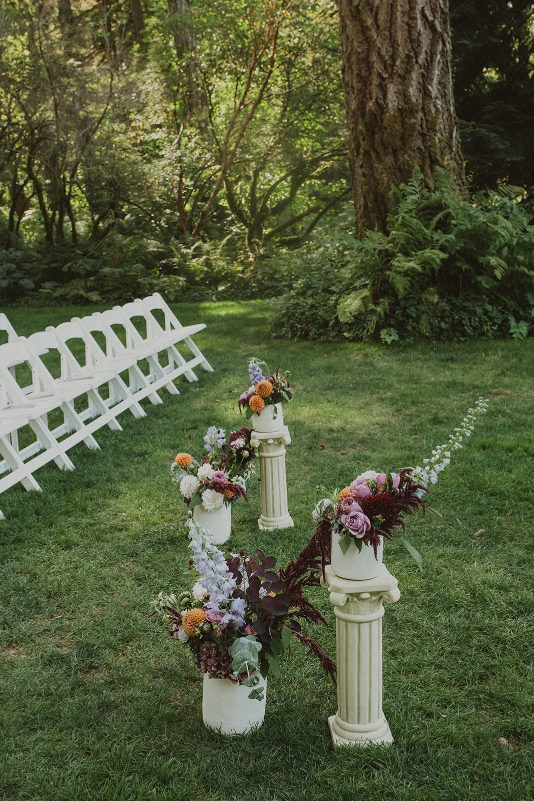 Arrangements in plum and apricot set on columns beside white folding chairs