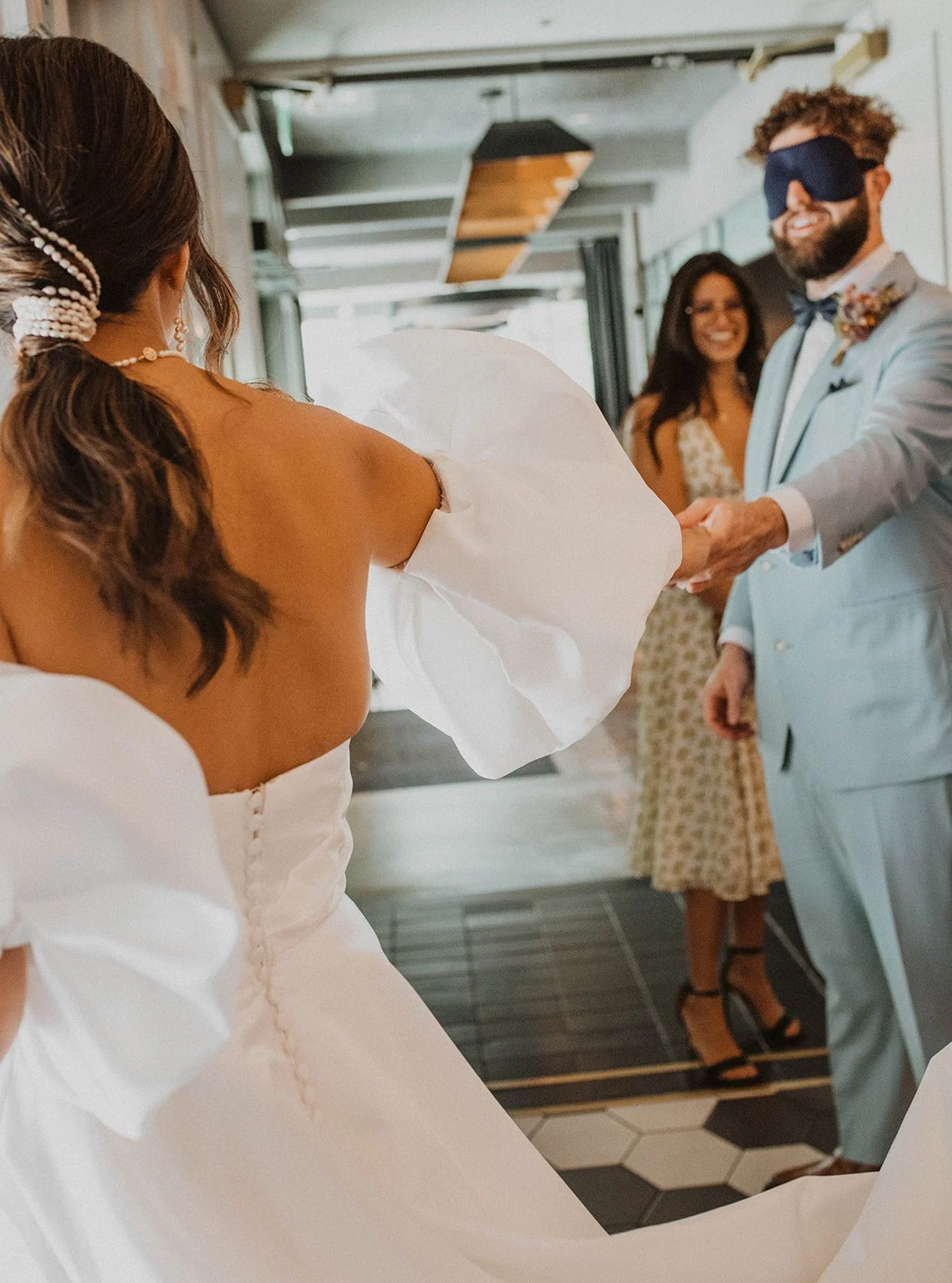 Groom wearing a sleep mask holding her hand while a friend watches