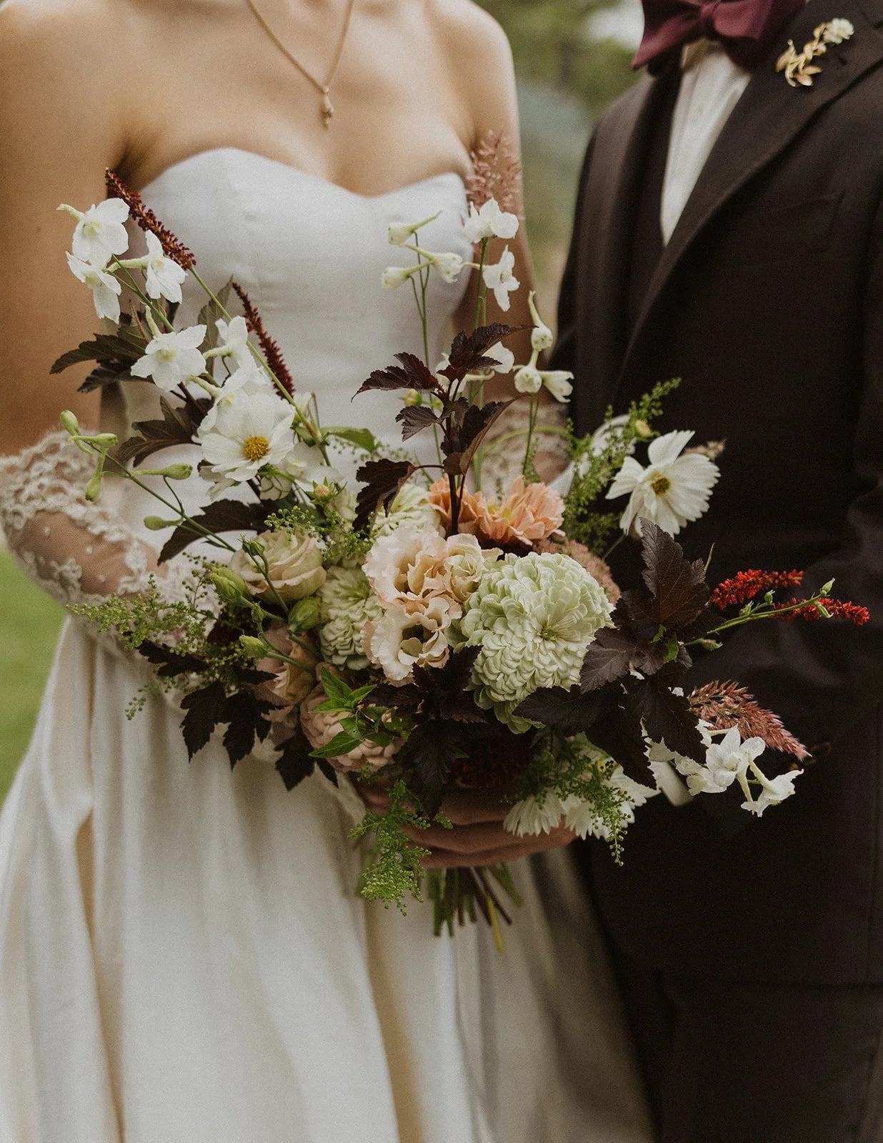 Loose bouquet of cosmos dahlias and dark foliage held between them