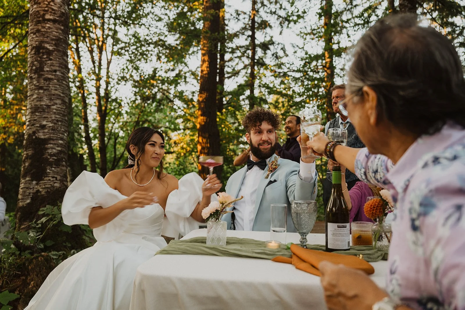 Bride and groom raising glasses with family during a celebratory wedding toast at their outdoor Bridal Veil Lakes reception.