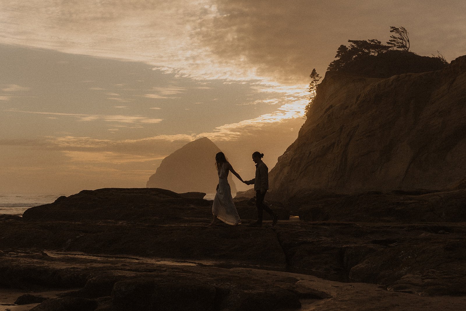 Silhouette of couple walking hand in hand across the rocky shoreline at Cape Kiwanda during sunset on the Oregon Coast