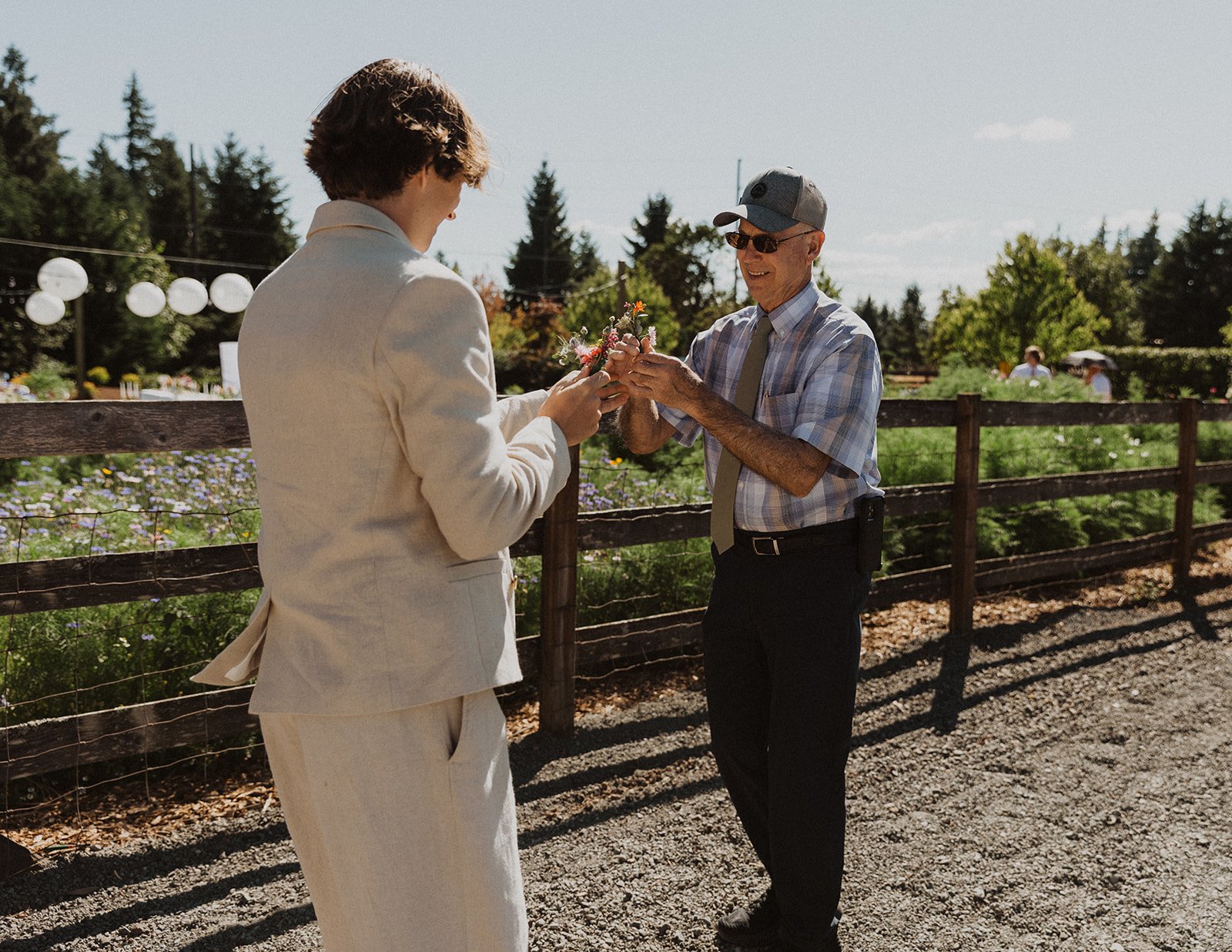 Groom receiving boutonniere from grandparent during outdoor garden wedding