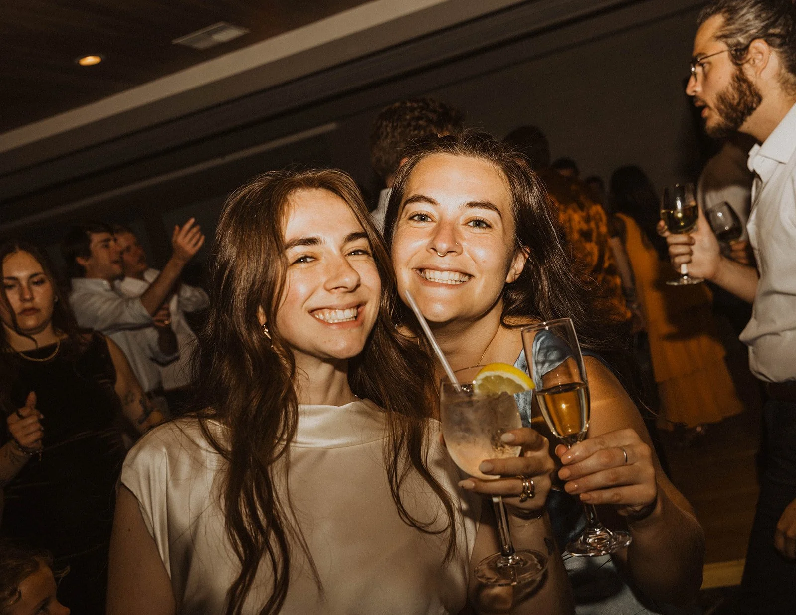 Two young women smiling and holding drinks at a party.