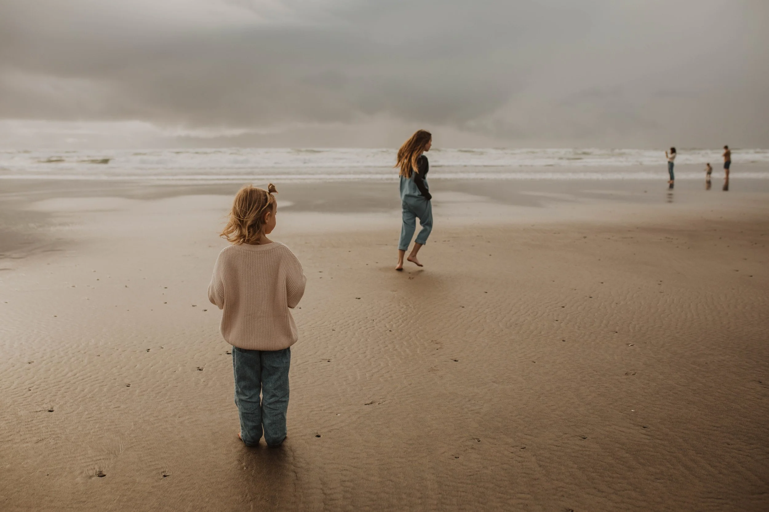 A group of people, including children and adults, enjoying a cloudy day at the beach with surf and wet sand.