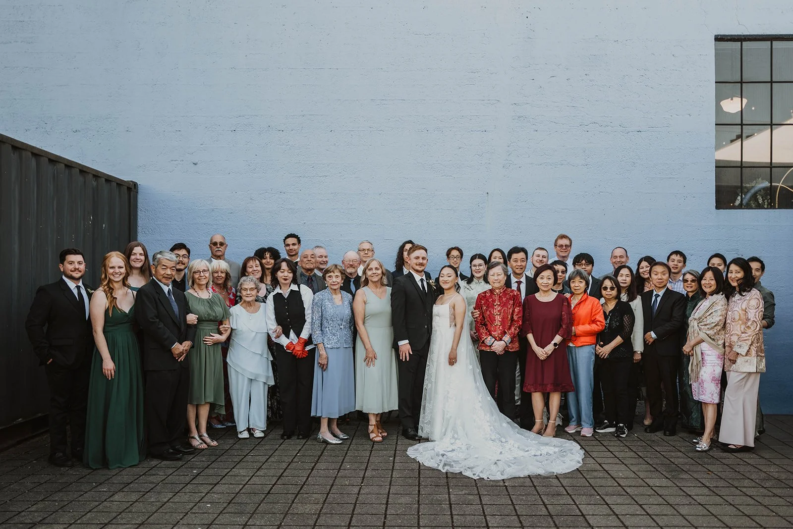 Bride and groom pose with extended family members for a large group portrait outside a Portland wedding venue after their ceremony.