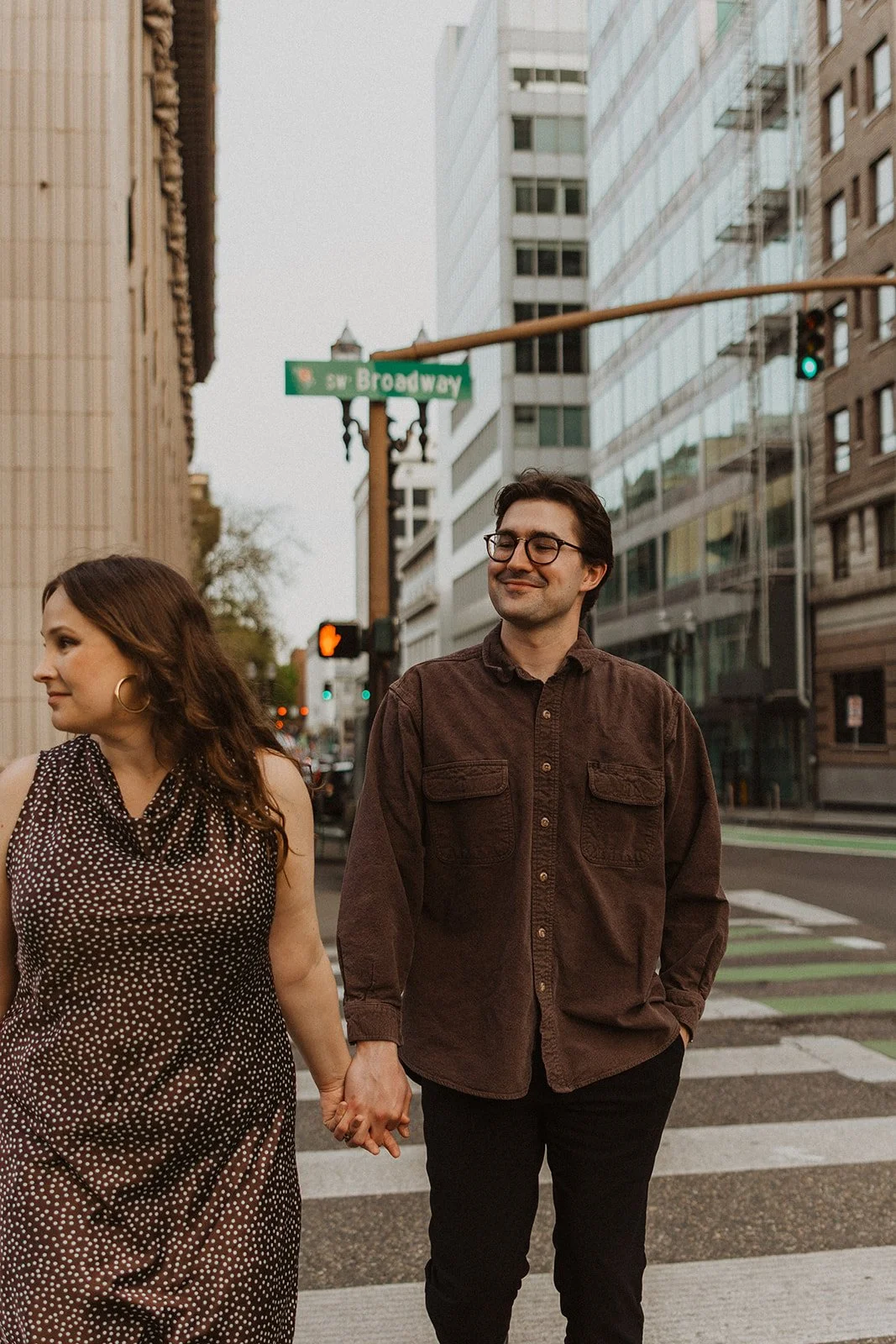 Couple holding hands and walking across a downtown Portland crosswalk on SW Broadway during an urban engagement session