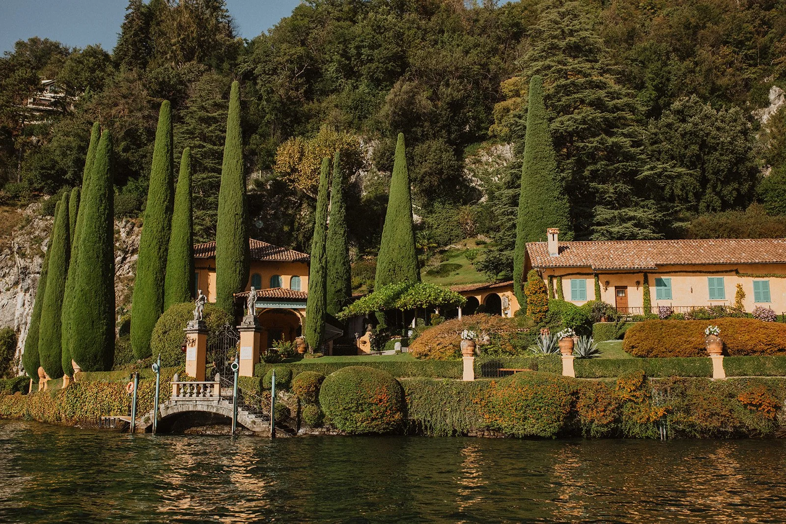 Elegant lakeside villa surrounded by cypress trees and manicured gardens along the shoreline of Lake Como, Italy.