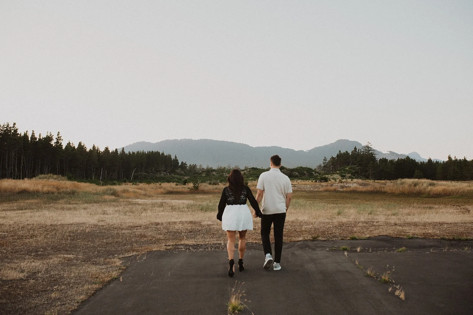 Couple walking hand in hand through an open field with mountains in the distance during an Oregon engagement session
