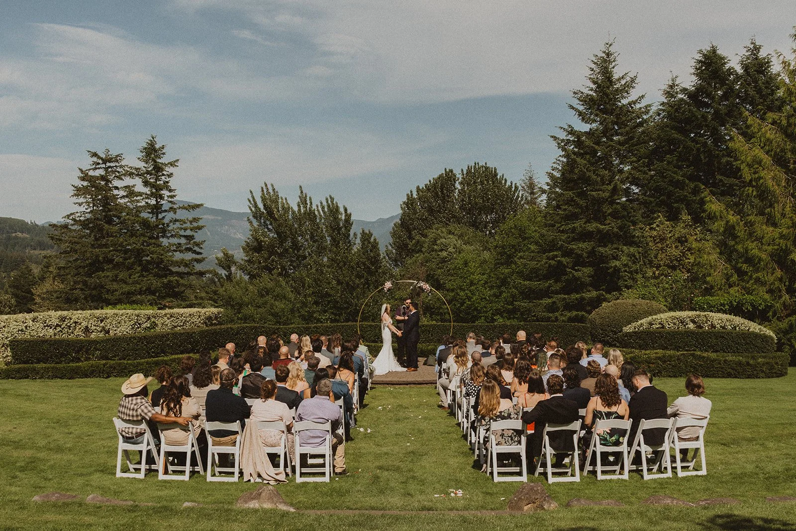 Wide view of an outdoor wedding ceremony at Skamania Lodge surrounded by gardens and Columbia River Gorge scenery.
