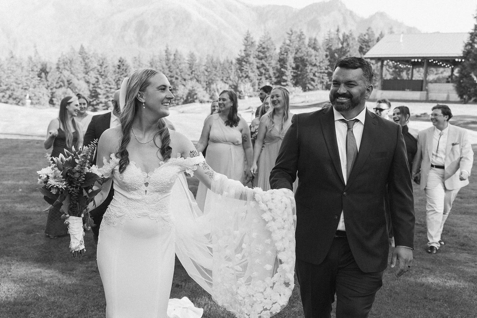 Newlyweds walking hand in hand after their outdoor ceremony at Skamania Lodge with guests following behind.