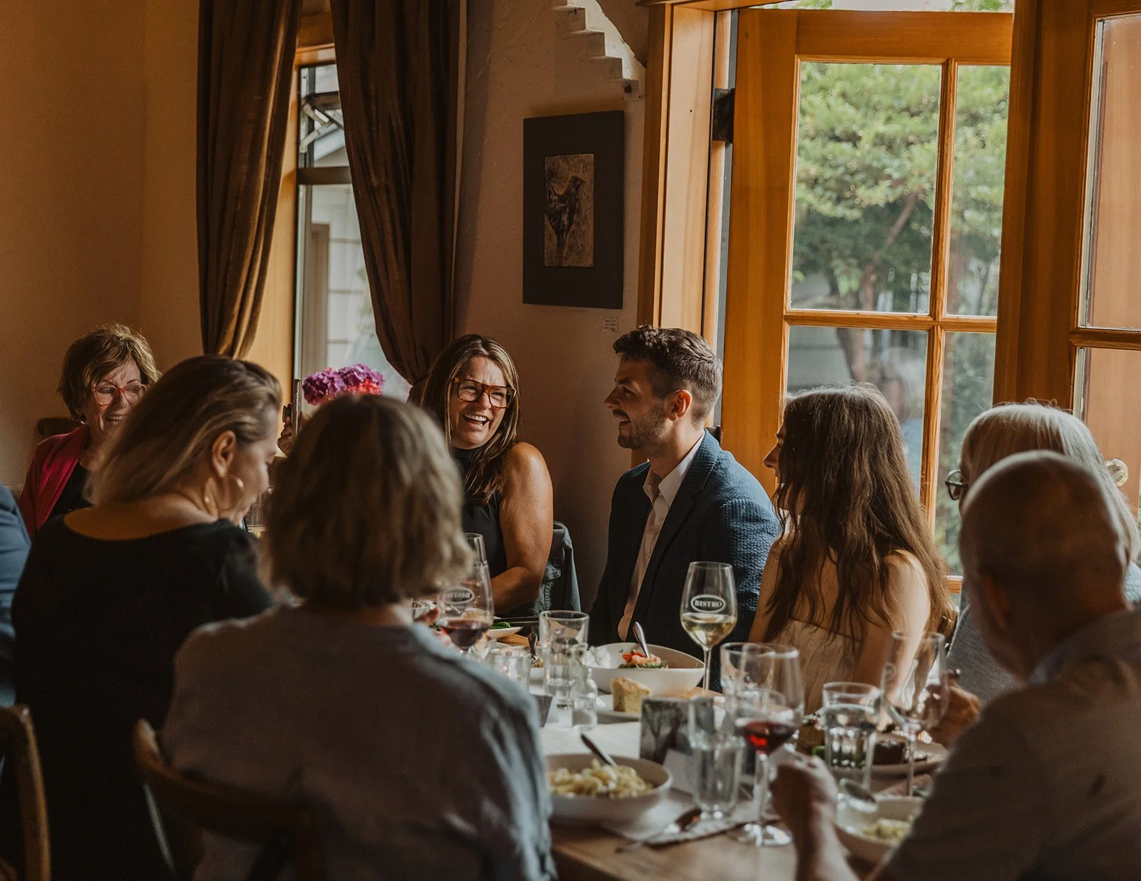 Couple laughing with friends and family during an intimate rehearsal dinner before their Cannon Beach wedding weekend
