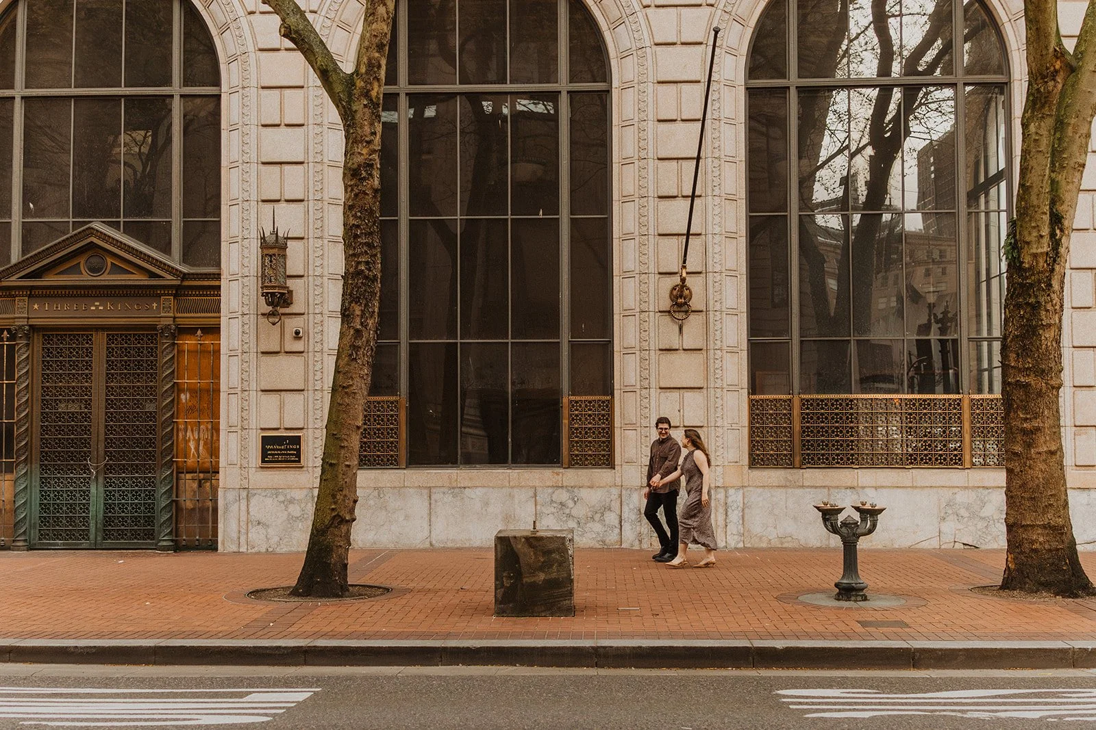 Couple holding hands while walking past a historic building in downtown Portland during an engagement session