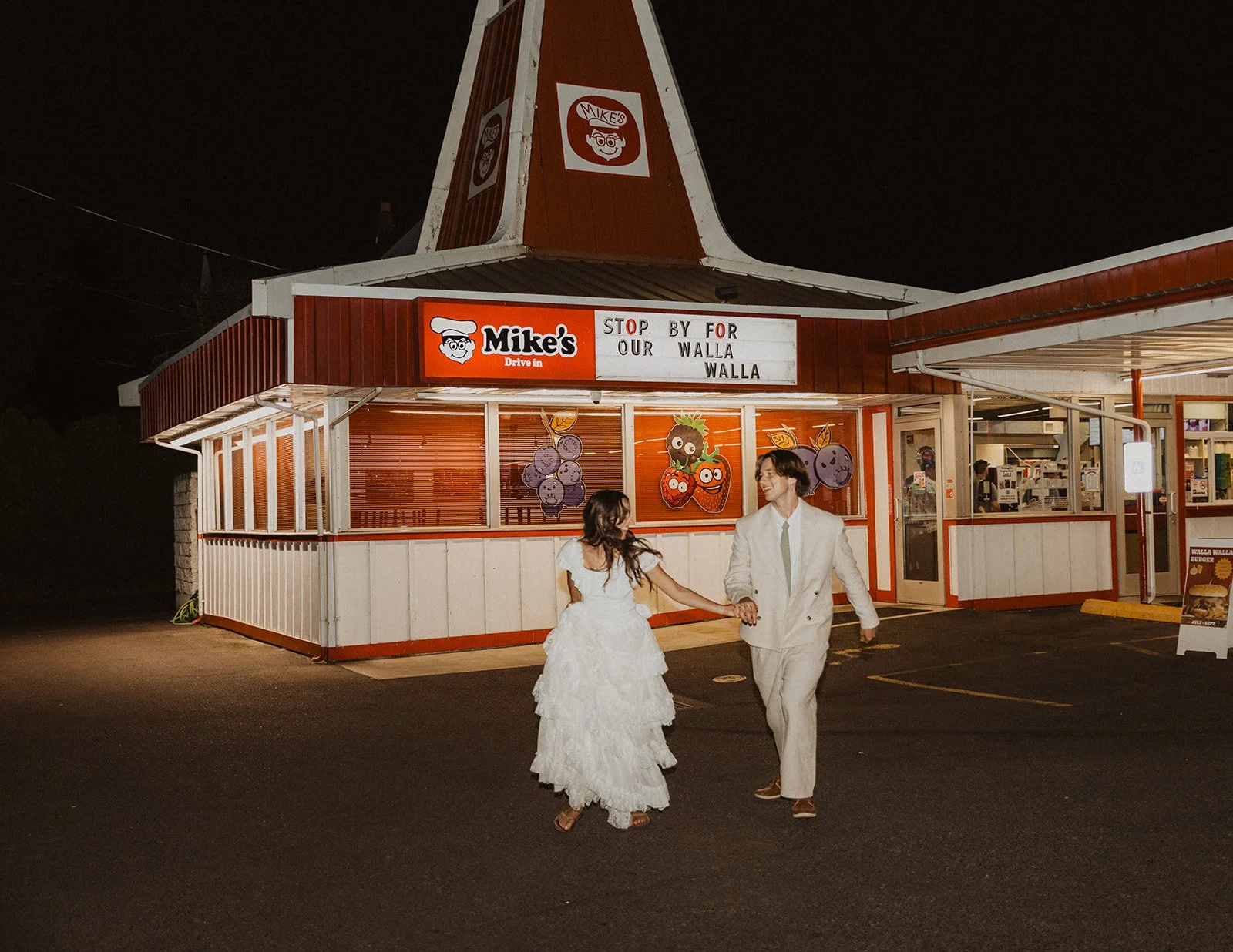 Just married couple walking hand in hand outside retro drive-in restaurant at night