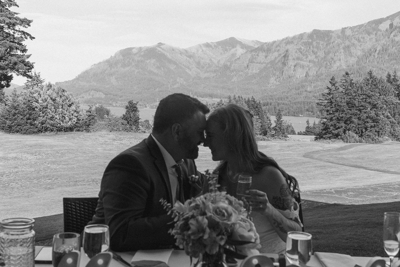 Bride and groom seated at their table with Oregon mountains behind them