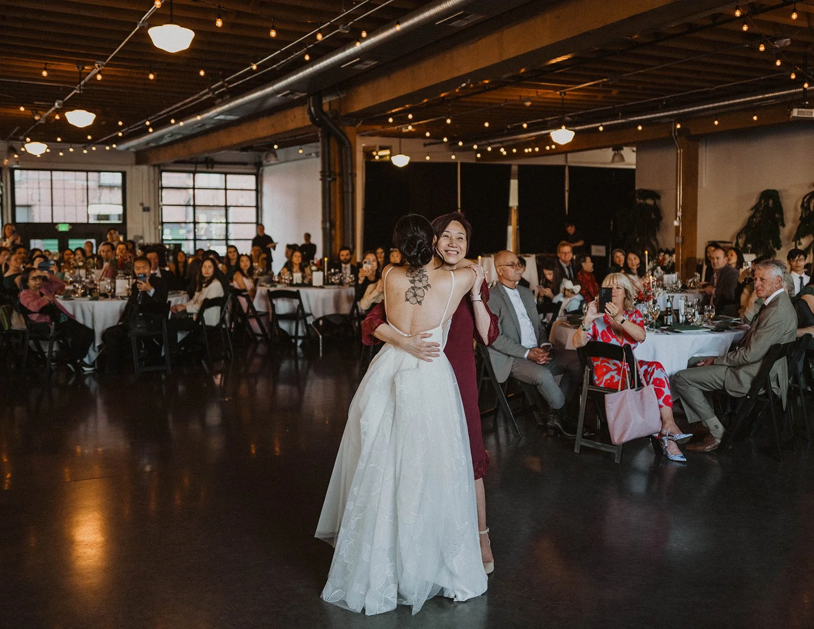 Bride embraces a family member during a special dance while wedding guests watch from reception tables at The Castaway in Portland.