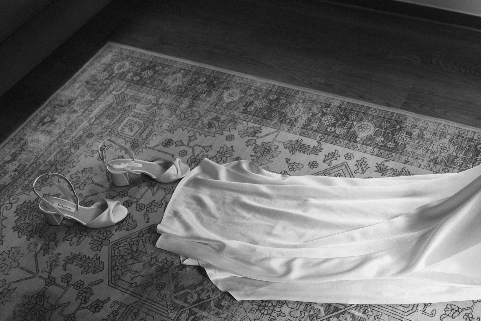White satin heels laid out beside the gown on a patterned rug