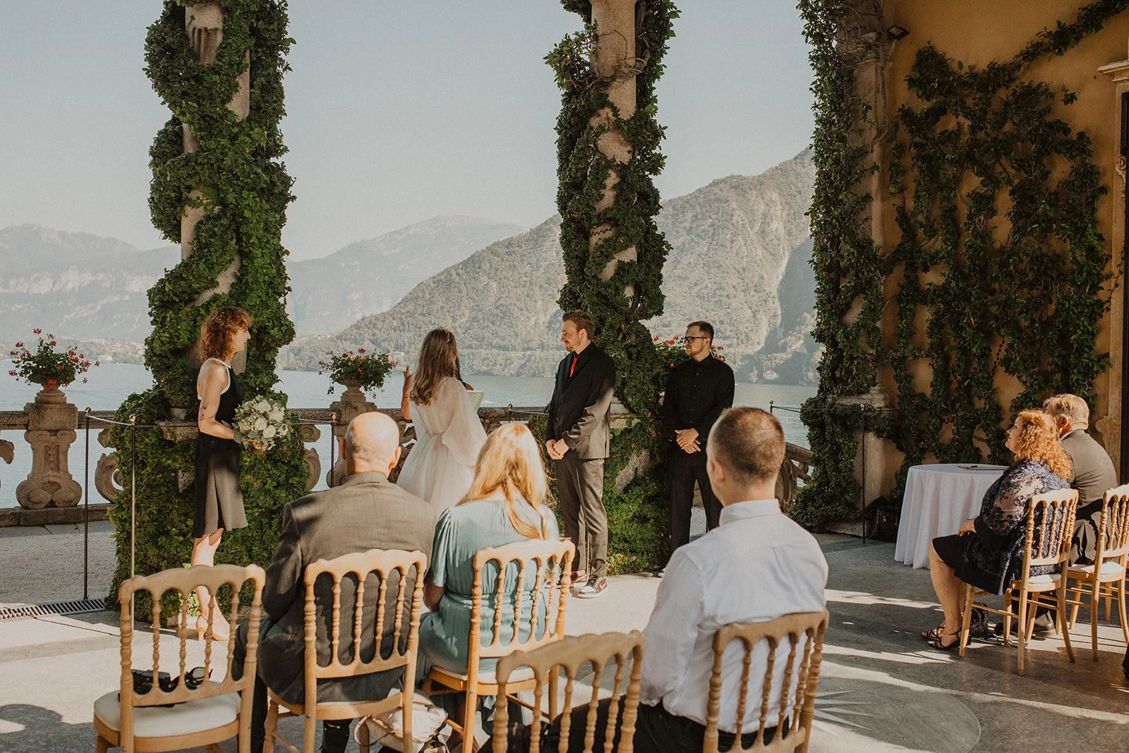 Guests watch as the couple exchanges vows during an intimate outdoor ceremony at Villa del Balbianello with panoramic Lake Como views.