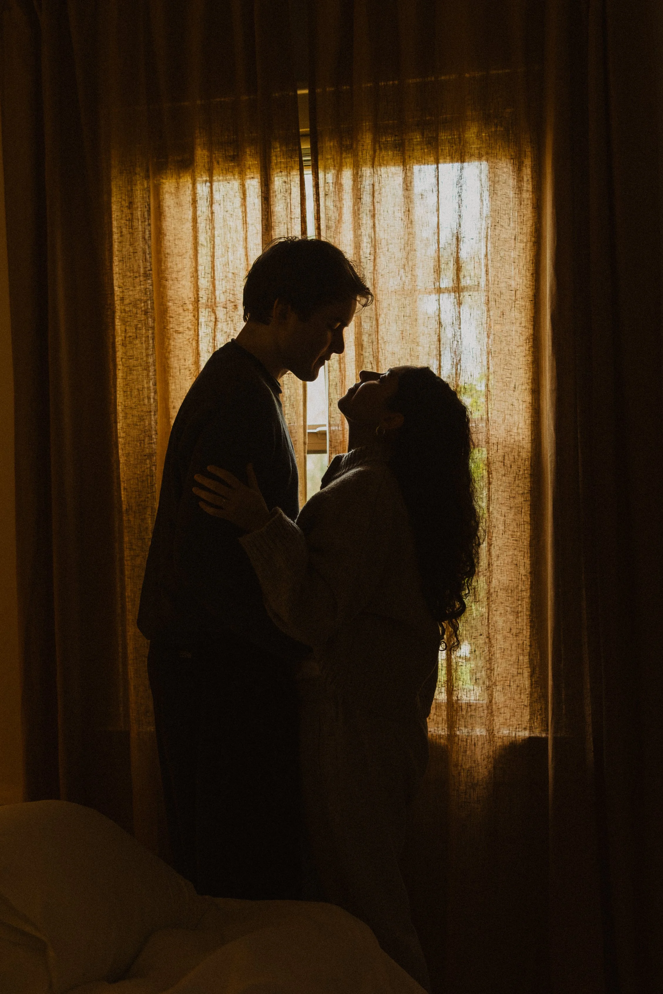 Silhouette of a couple embracing inside a room with sunlight filtering through curtains.