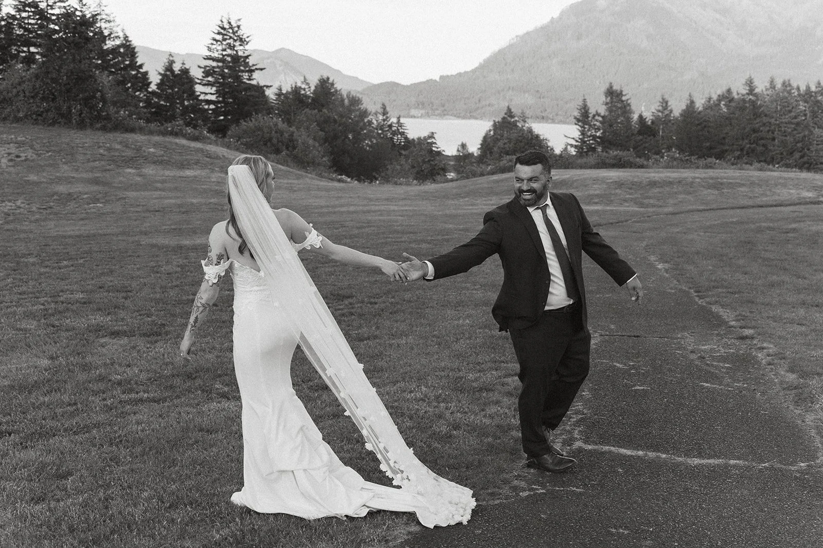 Bride and groom holding hands while laughing during playful wedding portraits overlooking the Columbia River Gorge at Skamania Lodge.