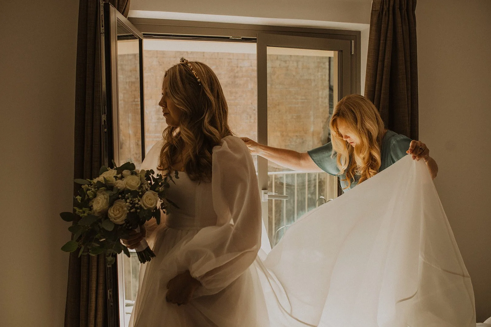Bride holding her bouquet while a family member helps arrange her wedding dress before a Lake Como elopement in Italy.
