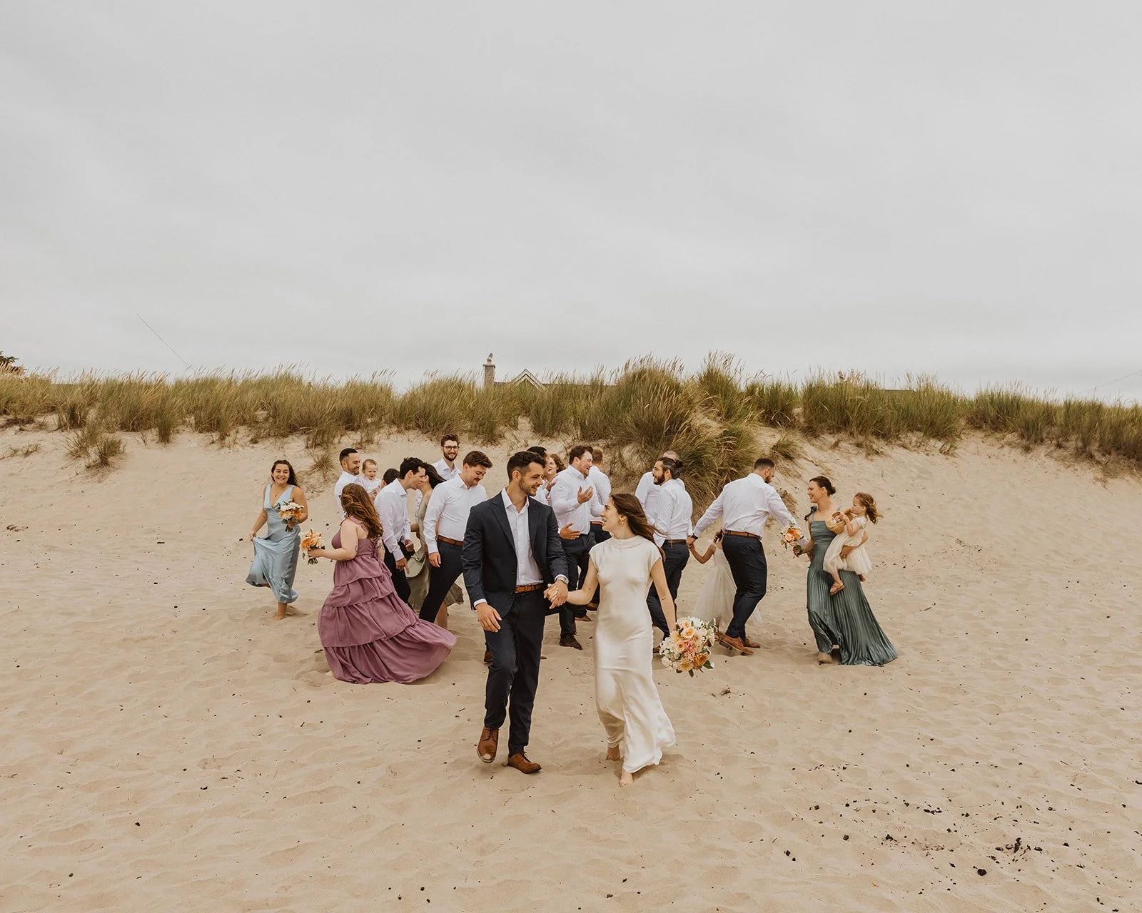 Bride and groom walking through the sand with their wedding party after their Cannon Beach ceremony