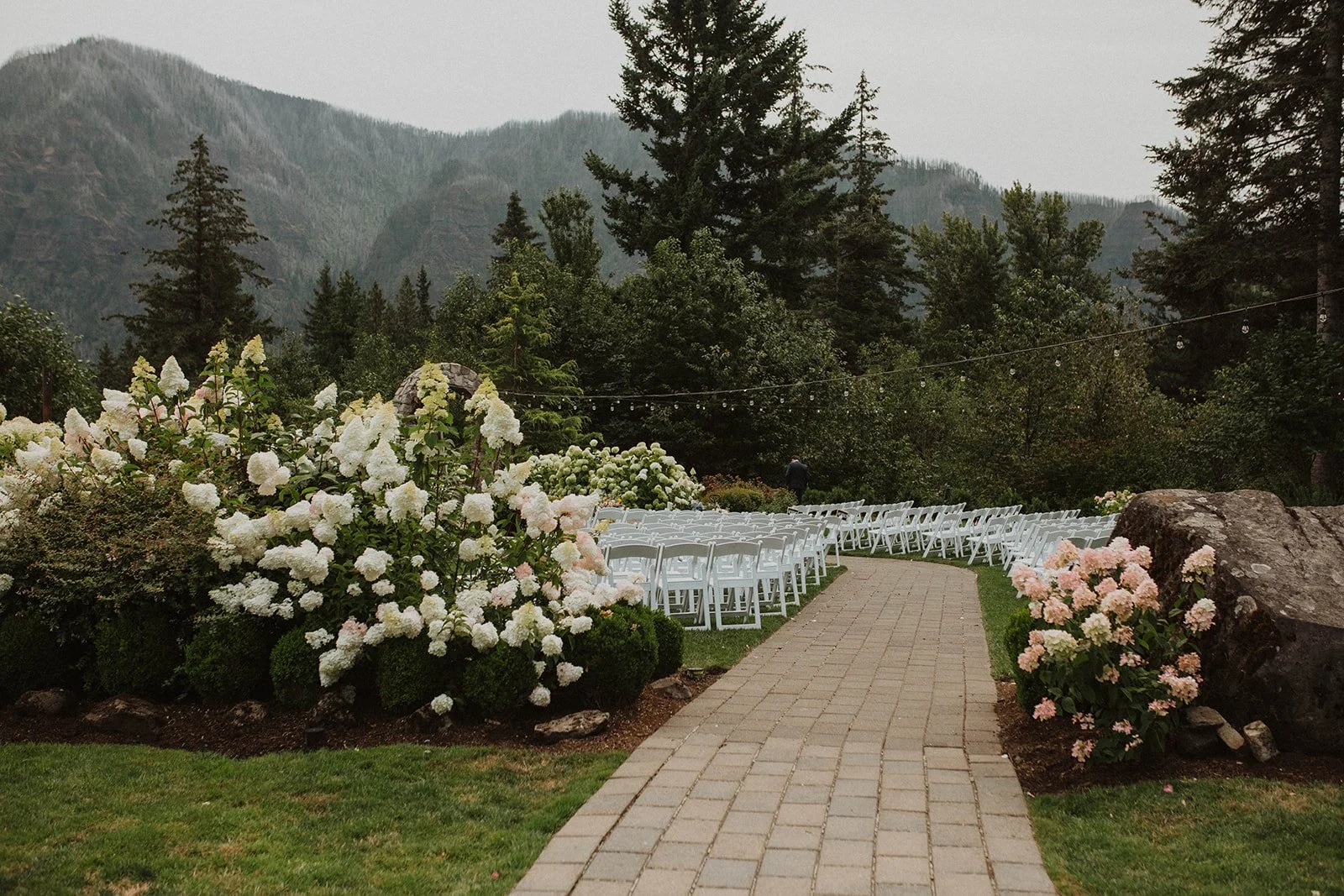 White chairs and hydrangea borders framing an aisle that faces the mountains