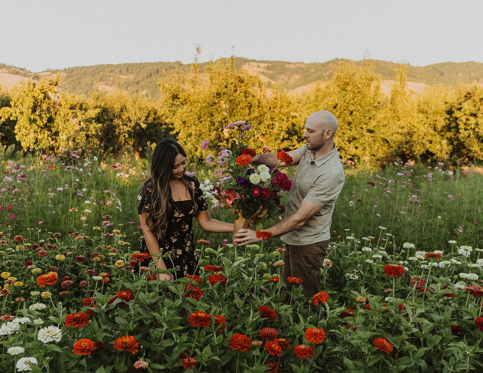 Couple creating a fresh flower bouquet among blooming zinnias and wildflowers during their engagement session