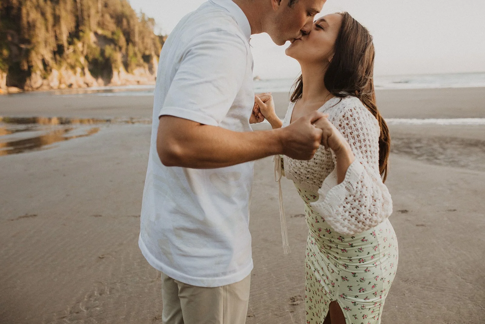 Couple walking along the sandy beach with coastal cliffs and forest during an Oregon coast engagement session