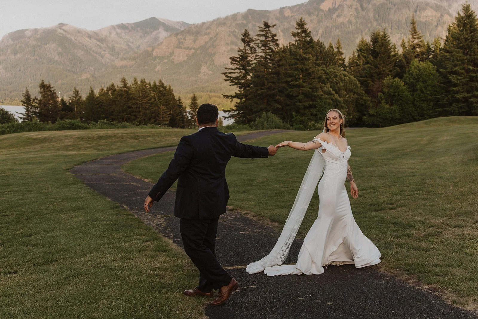 Newlyweds walking hand in hand with the Columbia River Gorge mountains behind them at Skamania Lodge.