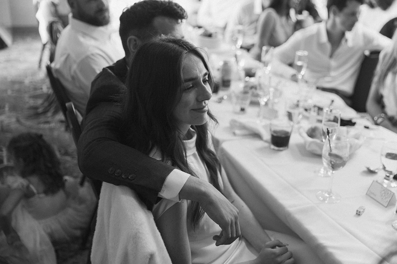 Black-and-white candid photo of a newlywed couple sharing a quiet moment together during their wedding reception dinner