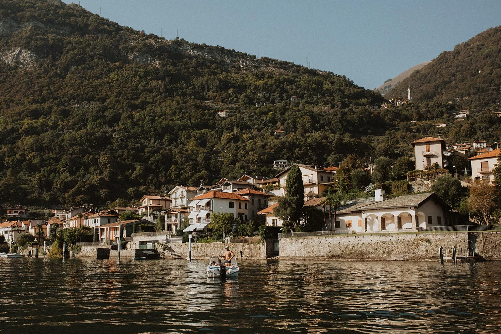 Scenic waterfront village and hillside homes viewed from a boat cruising across Lake Como in northern Italy.