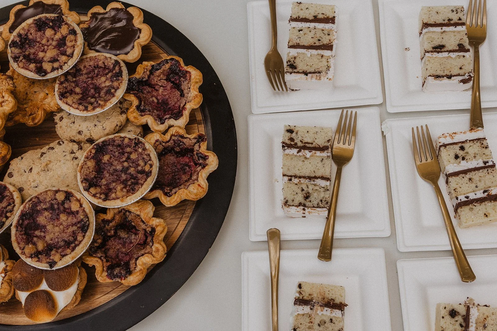 Dessert platter of berry tarts, cookies and sliced layer cake on gold forks